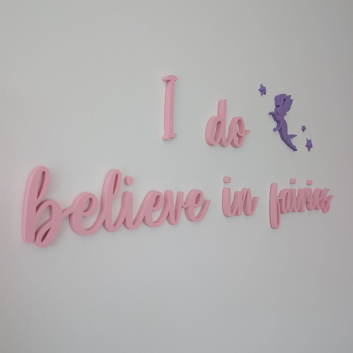 Decorative wall art with 'I do believe in fairies' text on a light gray background
