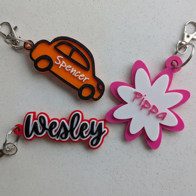 Three personalized keychains with names 'Spencer', 'Wesley', and 'Pippa' on a light gray background.