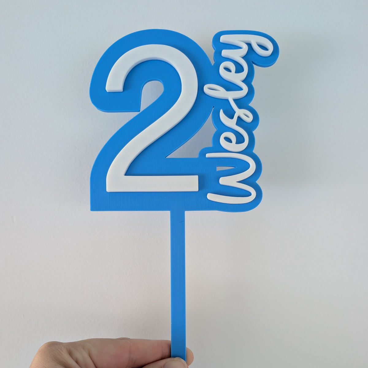 Blue cake topper with '2 Wesley' on a white background