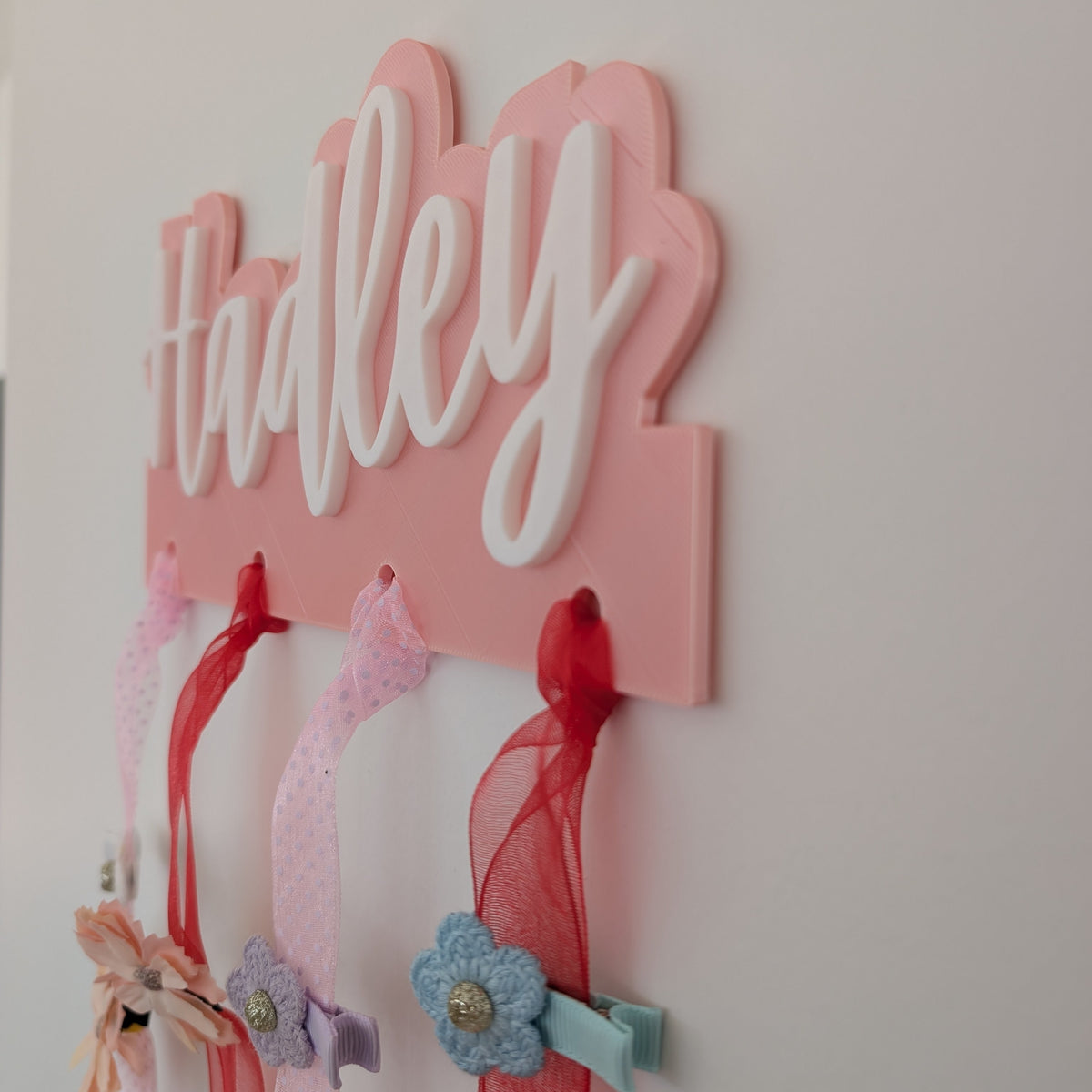 Pink decorative wall hanging with the name 'Hadley' and ribbons attached.