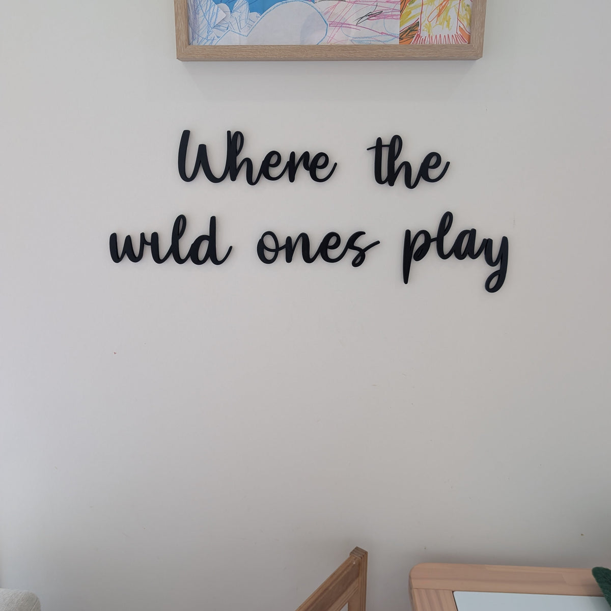 Decorative wall art with 'Where the wild ones play' text on a plain wall.
